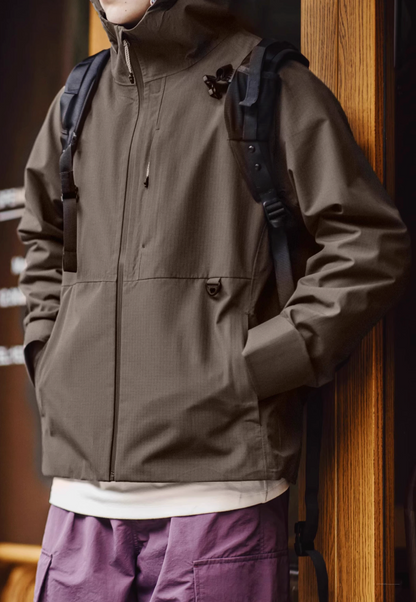 Khaki waterproof ripstop shell coat styled with backpack for outdoor commuting featuring clean silhouette and functional pockets