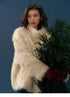 Model wearing Almond Aura Plush Coat holding winter greenery against blue backdrop