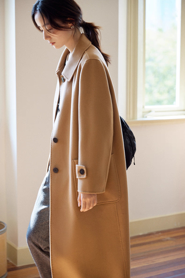 Side profile of woman walking in an almond-camel cashmere wool long coat with large patch pockets