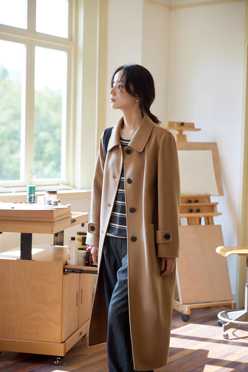 Three-quarter front view of almond-camel cashmere wool long coat, styled with striped knit and wide-leg trousers