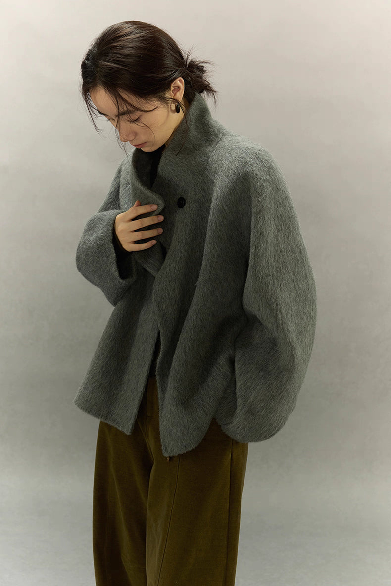 Sage gray alpaca wool jacket with asymmetric collar, model adjusting front closure
