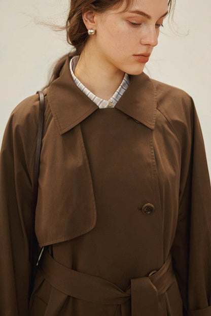 Dark brown trench coat close-up highlighting spread collar, button closure and smooth fabric texture