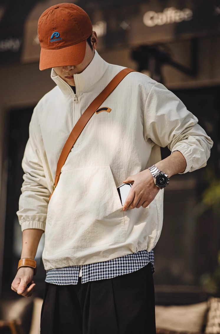 Model styling off-white lightweight anorak jacket with crossbody bag and cap