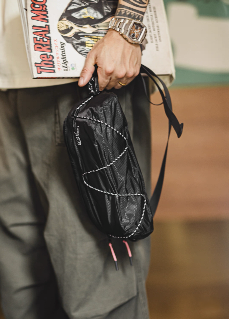 Hand-carrying AON Urban Air Sling black bag with magazine and watch