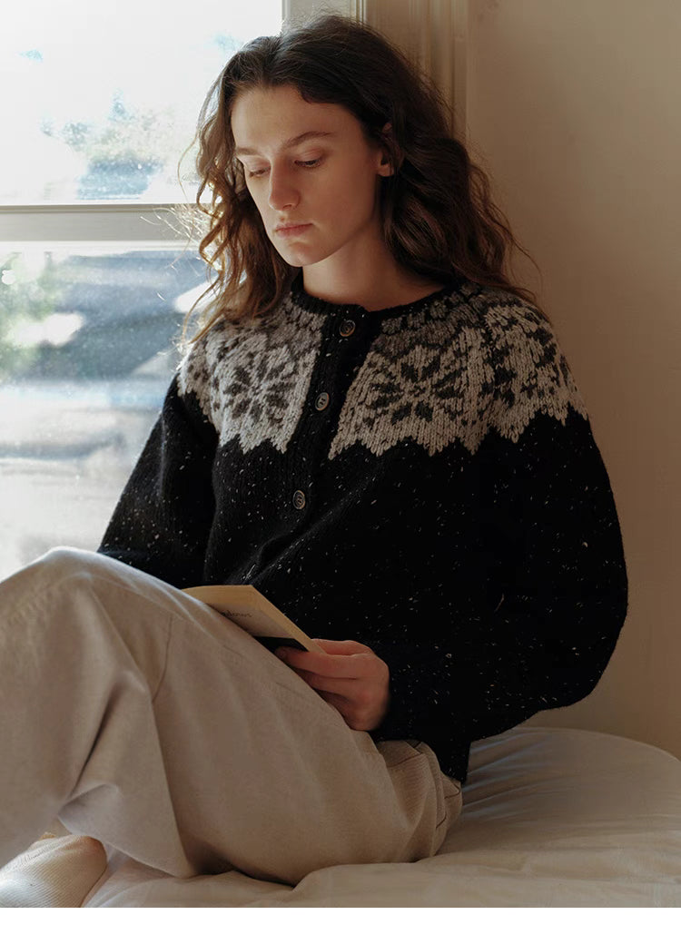 Black aran knit cardigan worn sitting and reading showing cozy winter styling and relaxed fit