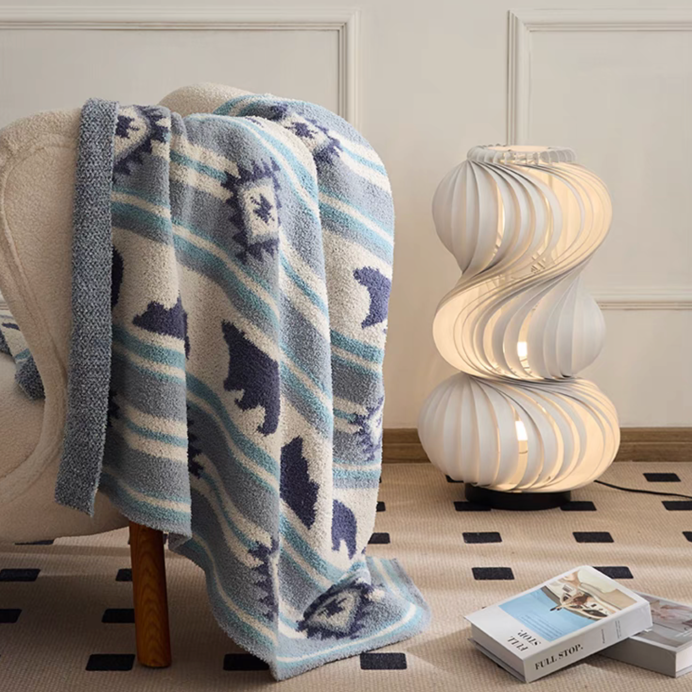 Blue Dream Bear blanket casually draped over armchair beside sculptural lamp in cozy living space