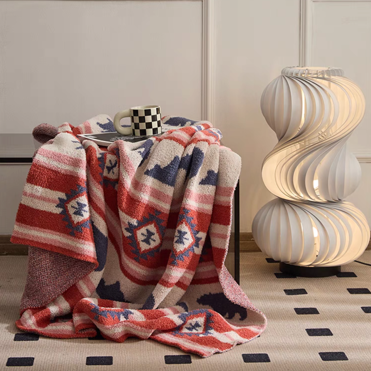 Red Embroidered Bear blanket draped over side table with checkered mug showing cozy indoor styling