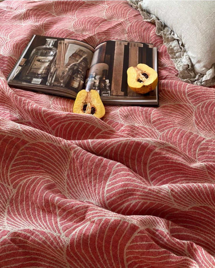Red ArcWeave linen cotton handloom throw blanket close-up showing woven arc pattern with open magazine and fruit on bed