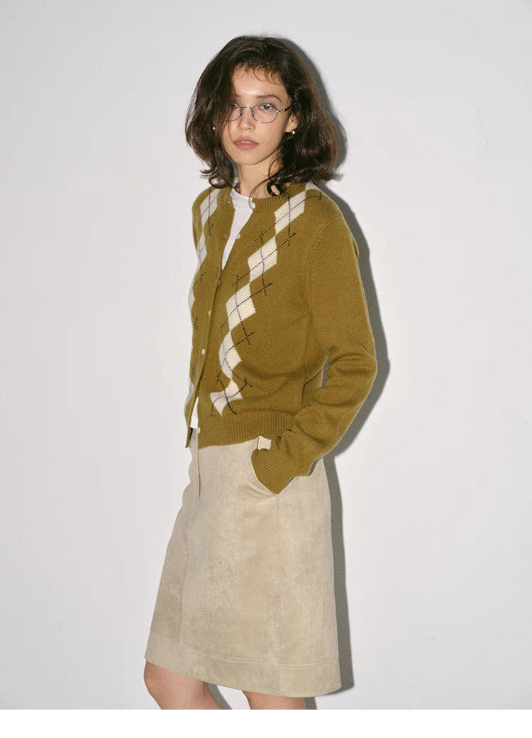 side view of model in olive argyle wool cardigan with beige skirt