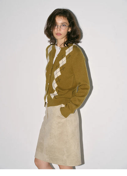side view of model in olive argyle wool cardigan with beige skirt