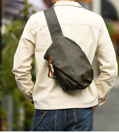 Man in beige jacket wearing army green leather sling bag across his back outdoors.