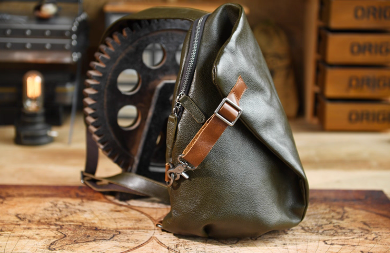 Side angle of army green leather sling bag showing zipper opening and brown strap accent near metal hook.