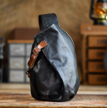 Front view of black full-grain leather sling bag with tan strap accent and soft matte finish.
