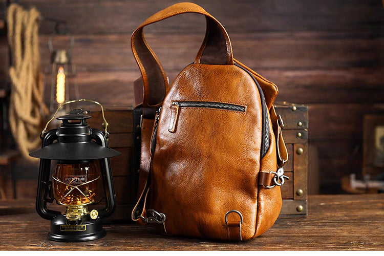Back view of caramel leather sling bag with rear zipper pocket beside vintage lantern.