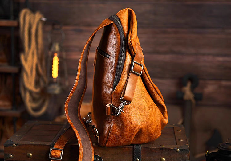 Caramel leather sling bag on wooden crate showing zipper opening and wide shoulder strap.
