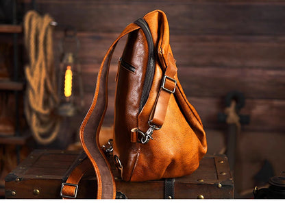 Caramel leather sling bag on wooden crate showing zipper opening and wide shoulder strap.