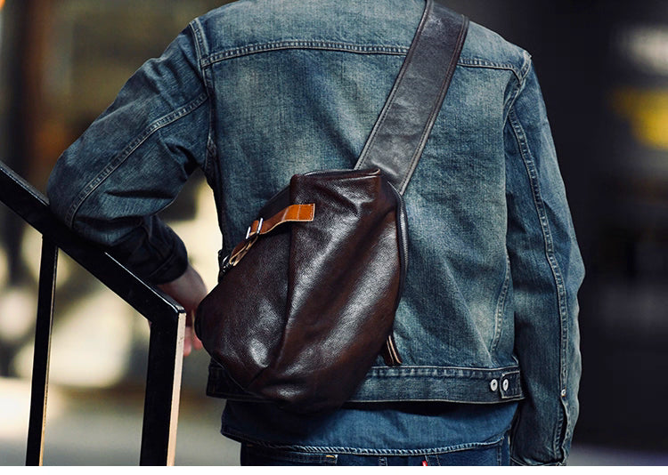 Man wearing dark brown leather sling diagonally across back with denim jacket.