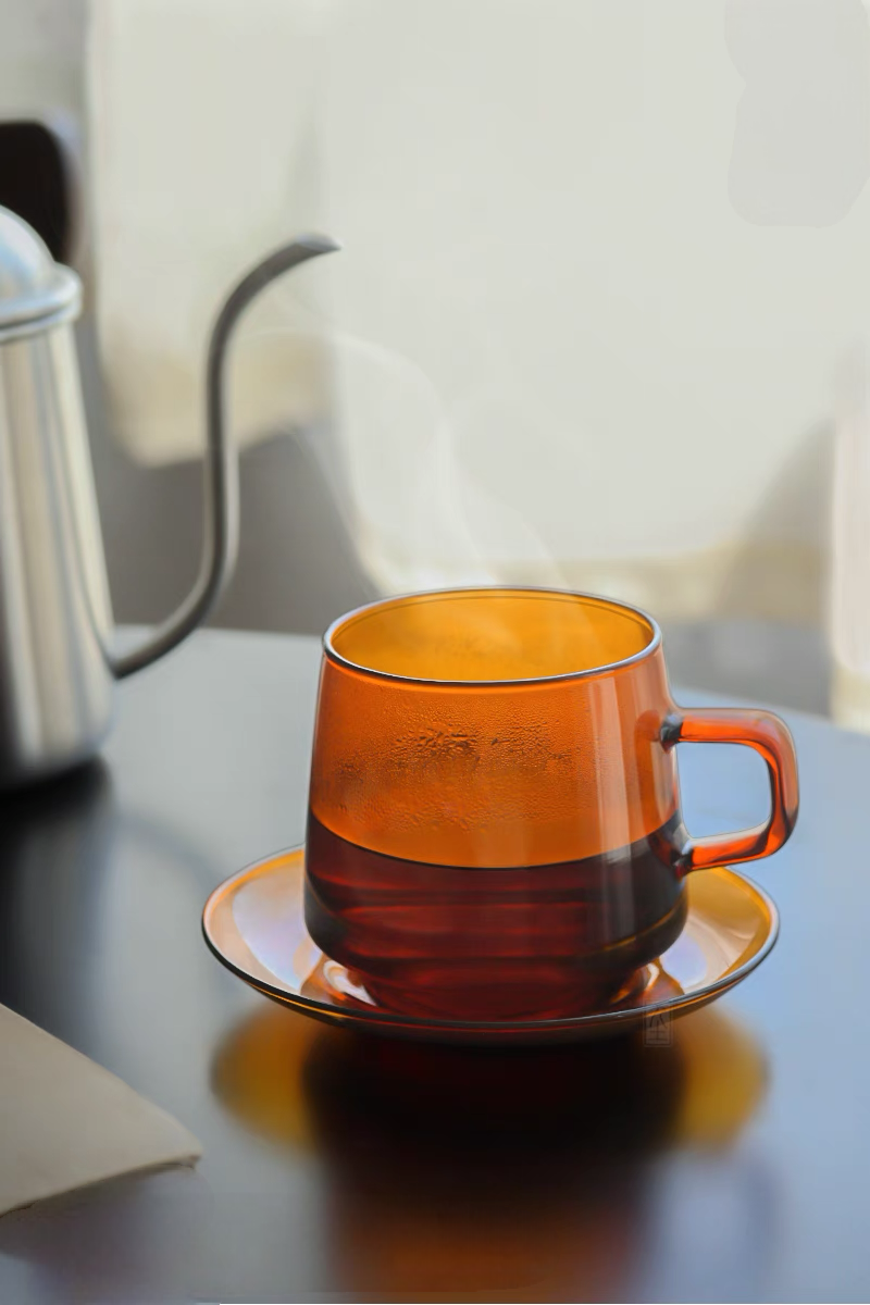 Amber Aurora Harmony glass cup and saucer with hot tea and visible steam in modern kitchen setting highlighting heat-resistant glass