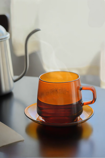 Amber Aurora Harmony glass cup and saucer with hot tea and visible steam in modern kitchen setting highlighting heat-resistant glass
