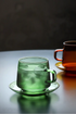 Green Aurora Harmony glass cup and saucer set with iced drink showing frosted condensation in modern lifestyle setting