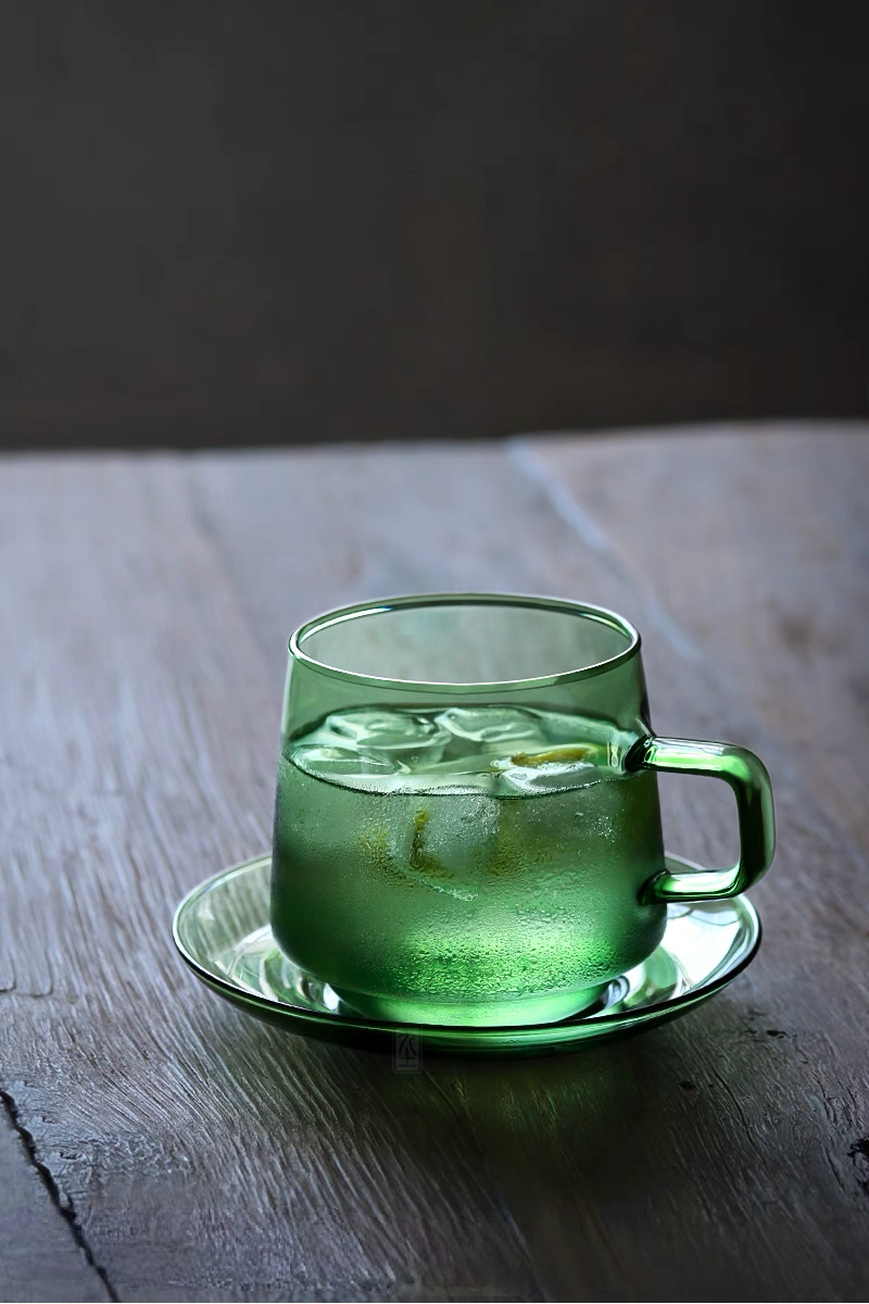 Green Aurora Harmony glass cup and saucer with iced beverage on wooden table showing textured condensation detail