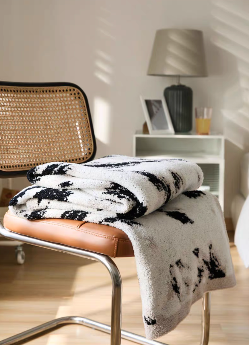 Folded black and white blanket placed on modern chair seat with visible layered folds and soft plush texture in warm interior