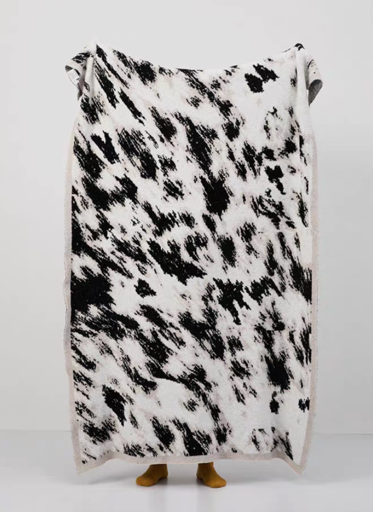Black and white abstract patterned blanket held up fully showing high-contrast brushstroke design against clean background