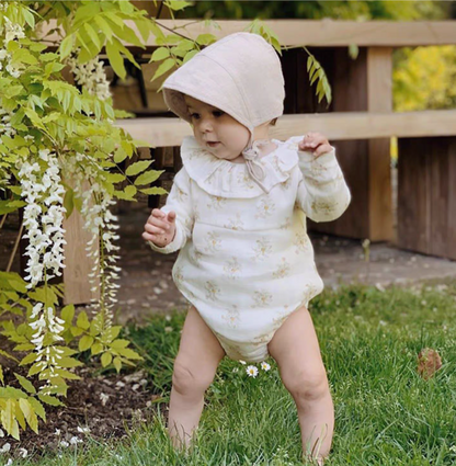 Baby wearing cream linen cotton sun hat walking on grass in garden floral outfit