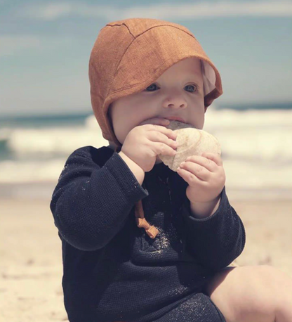 Baby wearing orange linen cotton sun hat at beach holding shell sunny lifestyle scene