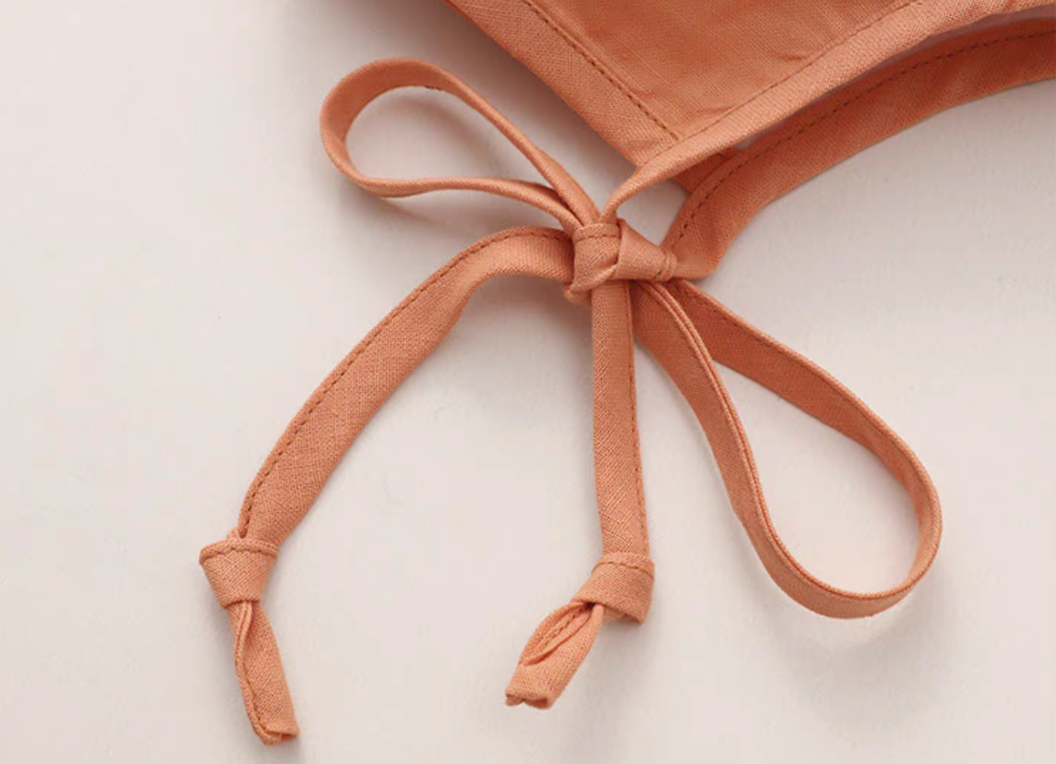 Close-up of orange baby sun hat tie straps showing knot detail and soft fabric finish
