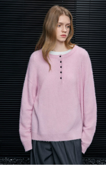 Woman wearing Baby Pink brushed alpaca Henley sweater with black buttons over a white tee and grey trousers