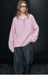 Model in Baby Pink fuzzy Henley pullover and glasses, one hand in pocket, with grey pleated trousers