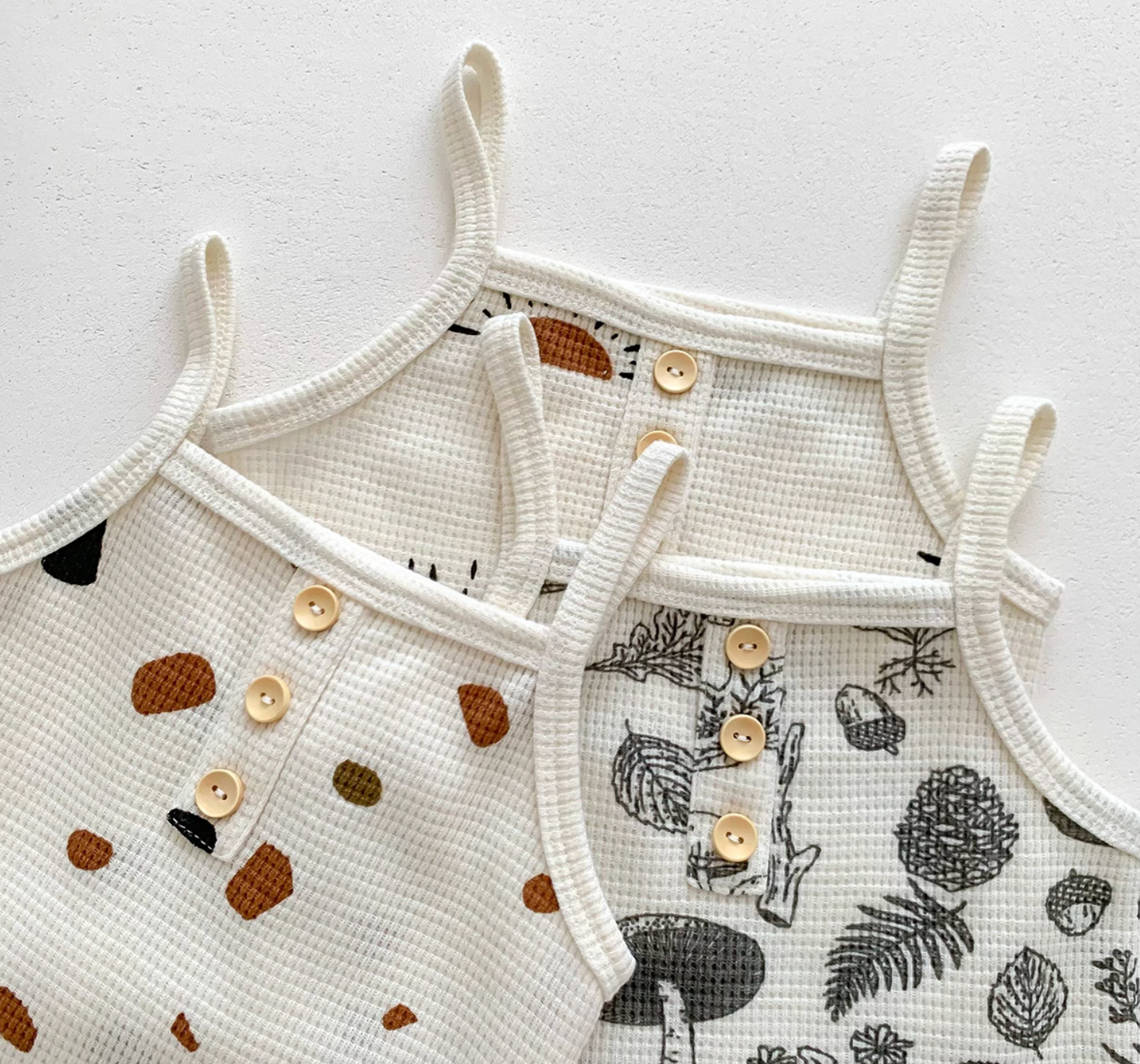 Three baby waffle knit camisole tops in sunshine, woodland, and stone prints