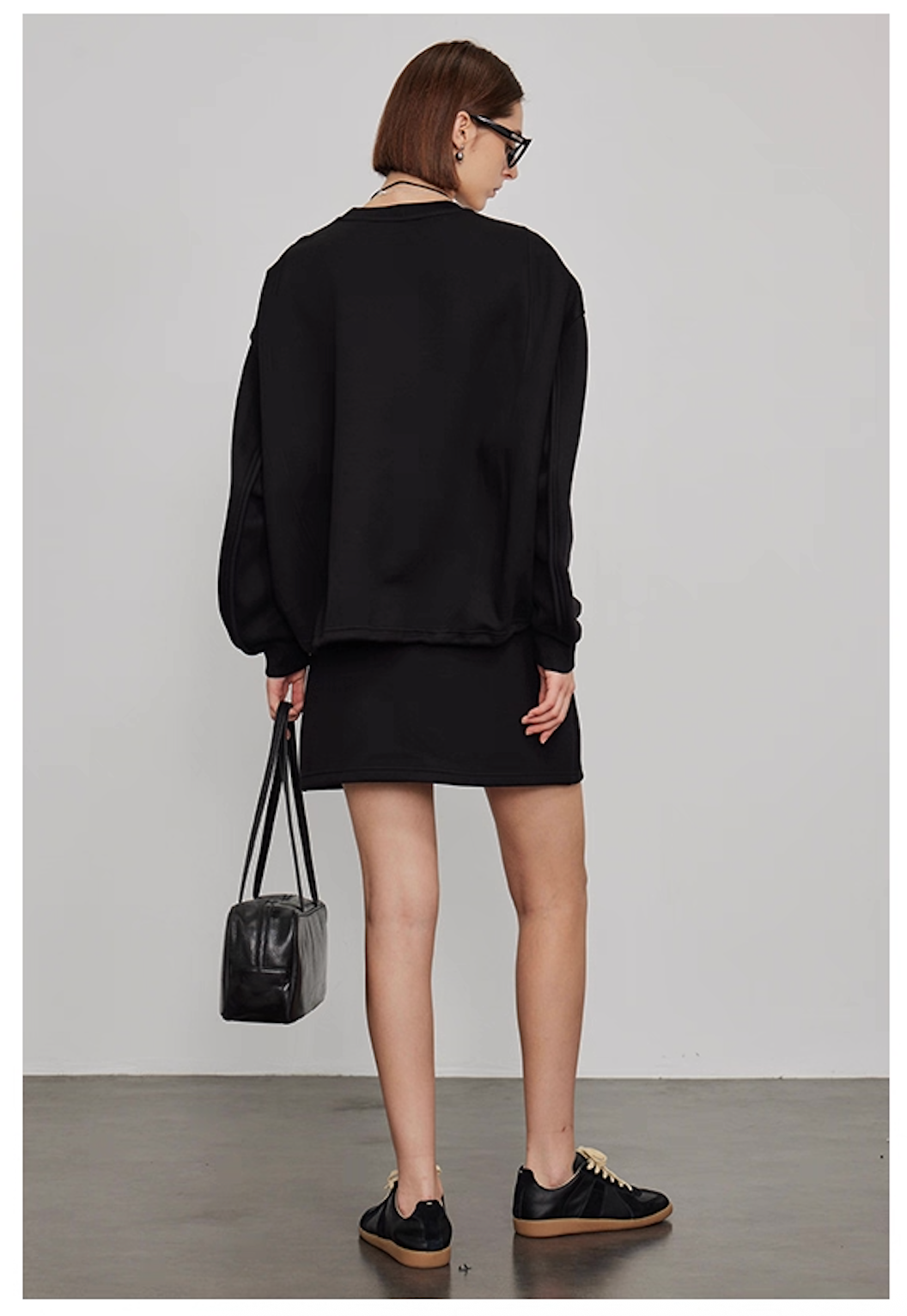 Back view of women’s oversized black sweatshirt with mini skirt casual loungewear