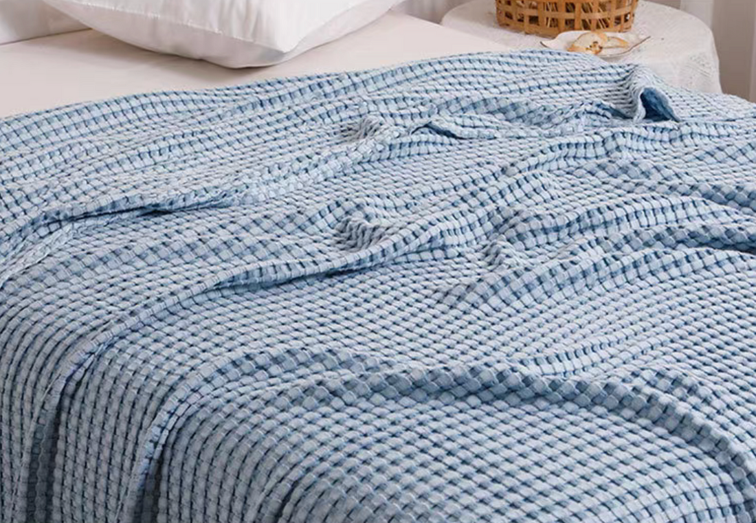 Blue bamboo cotton waffle knit throw blanket spread across bed showing breathable textured weave for cozy all-season comfort