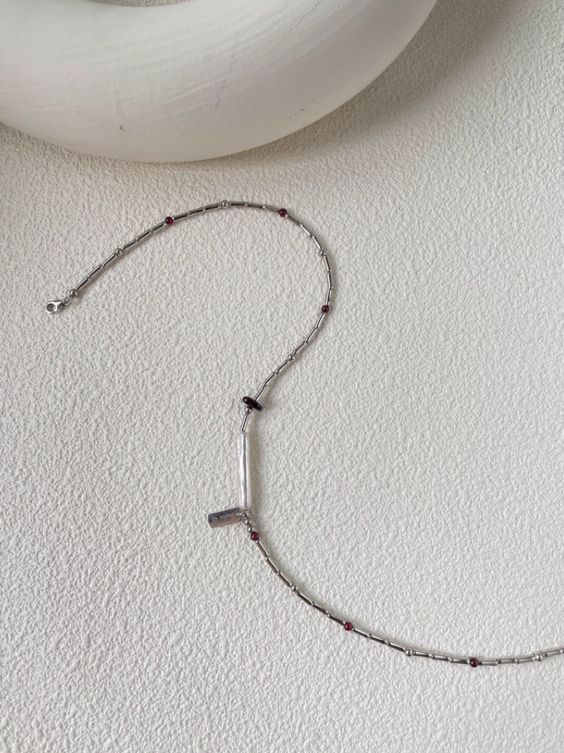 Baroque Elegance Layered Necklace in garnet with baroque pearl and silver chain displayed on textured surface