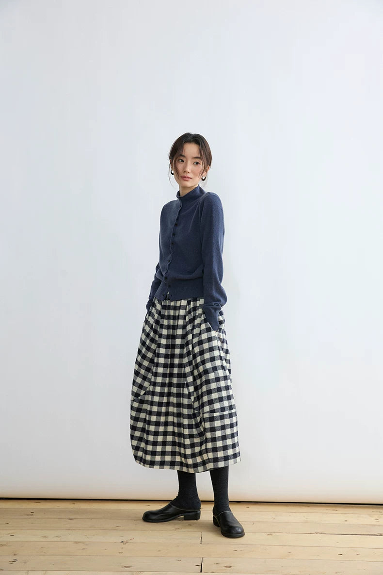 Angled view of a black and cream gingham midi skirt with hands in its side pockets