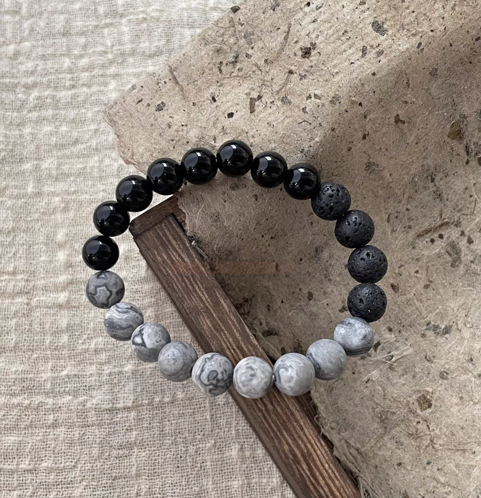 Black Beach Onyx Volcanic Stone Bracelet with black onyx, volcanic stone and gray map stone beads on textured wood surface