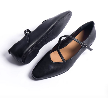 Black ballet flats showing the stitched leather sole and the crossed buckle strap