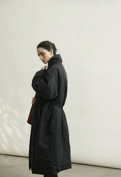Back-side view of a Black belted down coat showing the stand-up collar and calf length