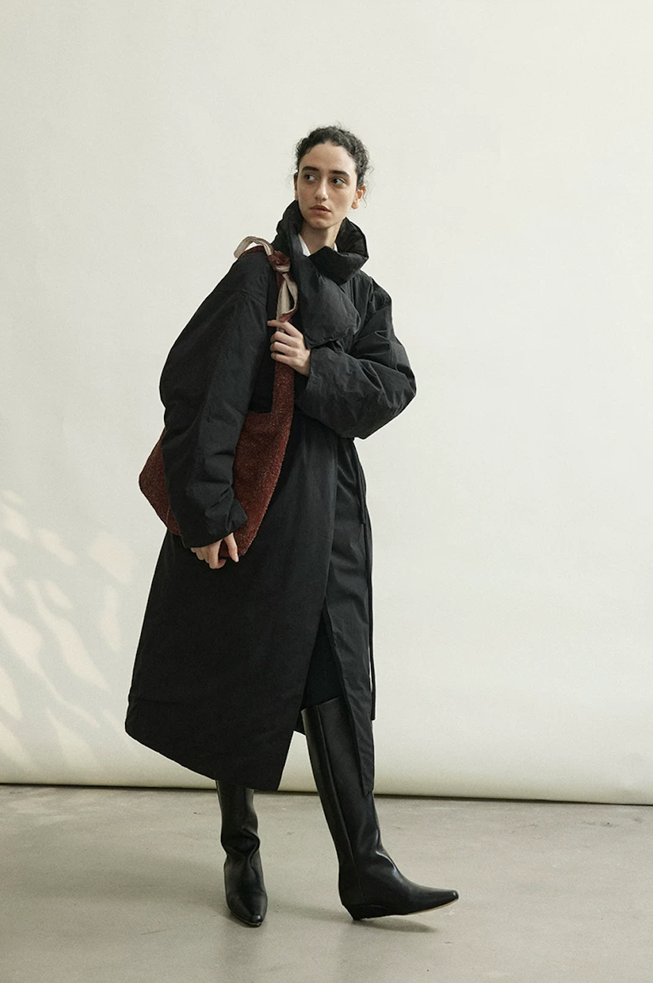 Black long down coat with the collar turned up, wrapped and belted, worn with tall boots