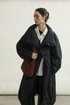 Black long cotton down coat with oversized padded lapel collar, worn loosely closed