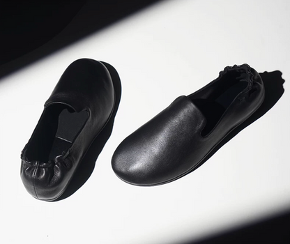 Pair of Black lambskin slipper loafers with gathered elastic heels, angled view in dramatic light