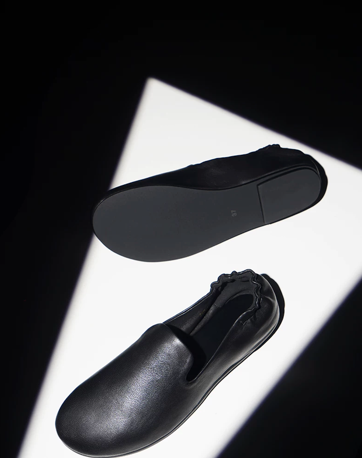 Black slipper loafers showing the slim black outsole and the soft lambskin upper