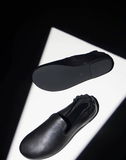 Black slipper loafers showing the slim black outsole and the soft lambskin upper