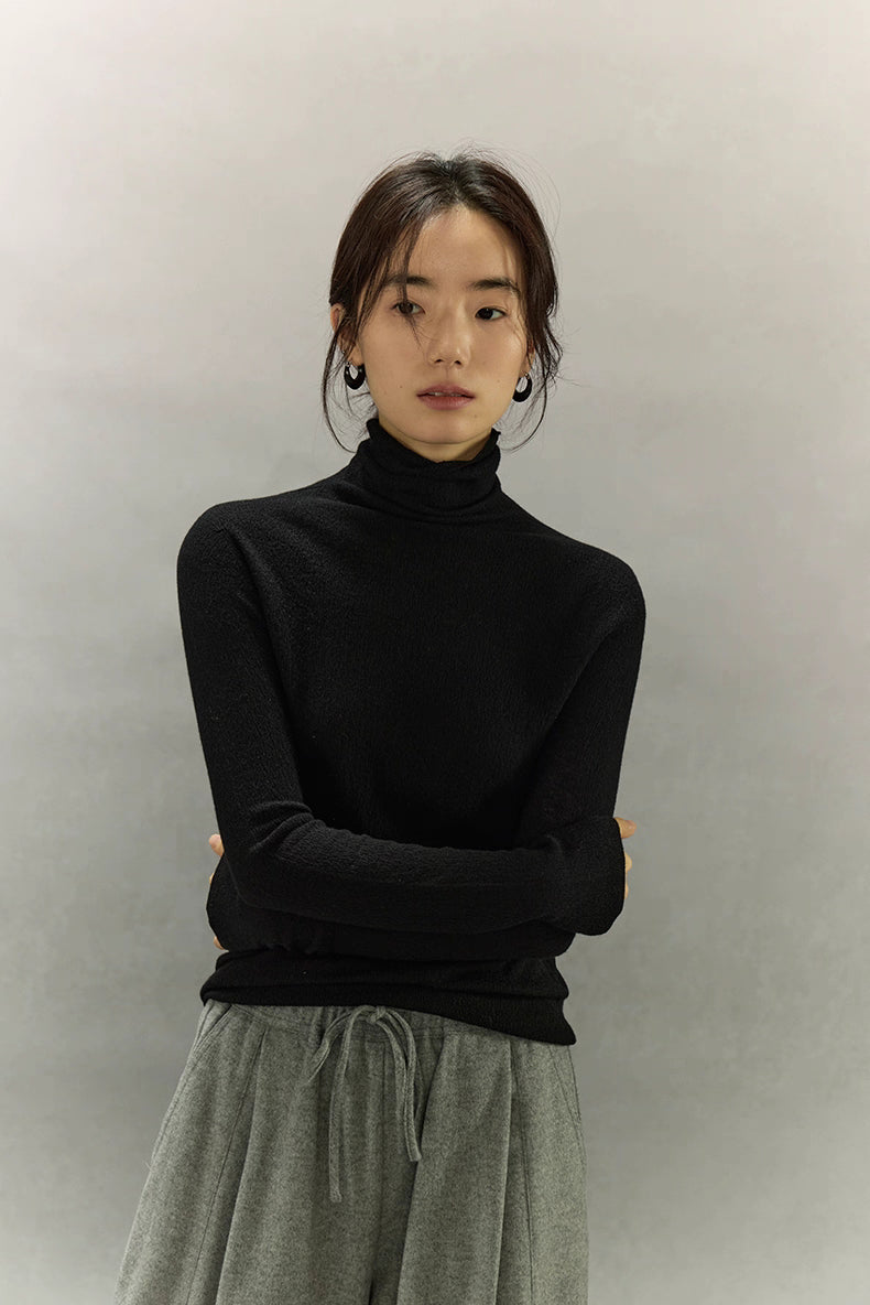 Black seamless turtleneck with crossed-arms pose, slim fit silhouette.