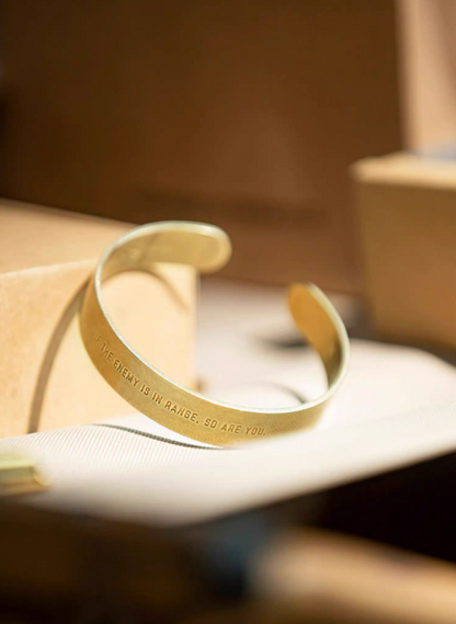 Brass cuff bracelet with engraved message placed on surface in warm lifestyle setting