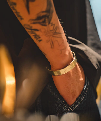 Person wearing brass cuff bracelet on wrist showing engraved message in natural color finish