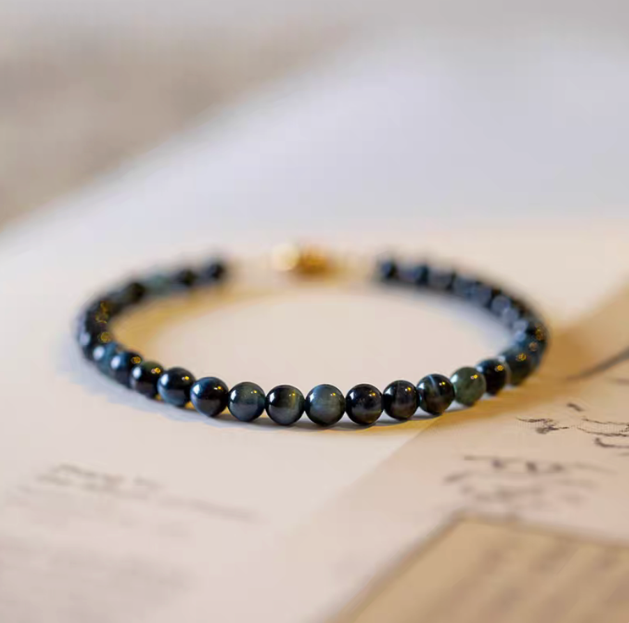 Blue Tiger’s Eye bracelet with natural blue round beads arranged in a circle on paper surface with soft document background