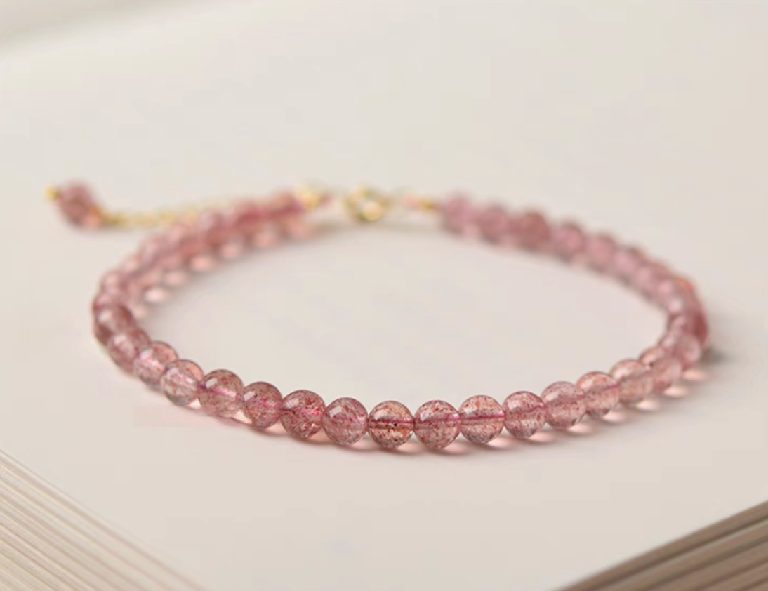 Pink strawberry quartz bead bracelet placed on a book in soft minimal aesthetic setting